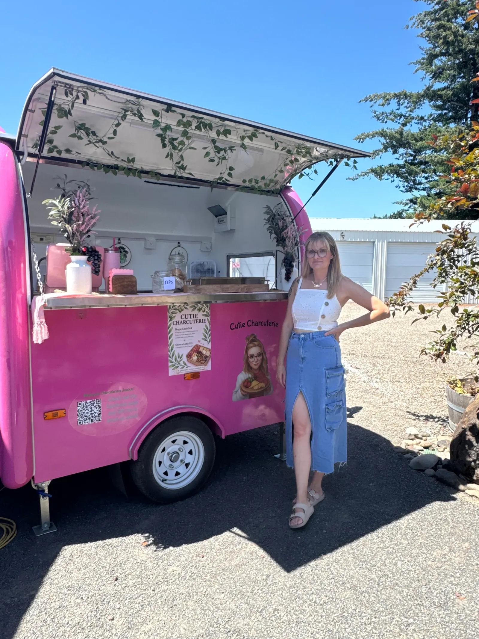 Jessica standing beside the bright pink Cutie Charcuterie trailer with its serving window open